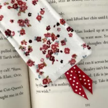 detailfoto van een witte boekenlegger met kleine rode bloemtjes en groene blaadjes. Met een rood lintje met stippen aan de onderkant