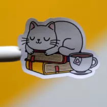 sticker van een kat liggend op twee boeken met daarbij een kopje thee