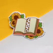 sticker met opengeslagen boek met daarin een boekenlegger met zonnebloemen, aan de buitenkant van het boek zie je ook zonnebloemen