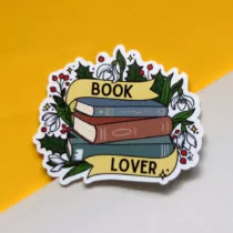 vinyl sticker met daarop een stapel boeken met een lint waarop staat book lover, met daaromheen verschillende winterse plantjes